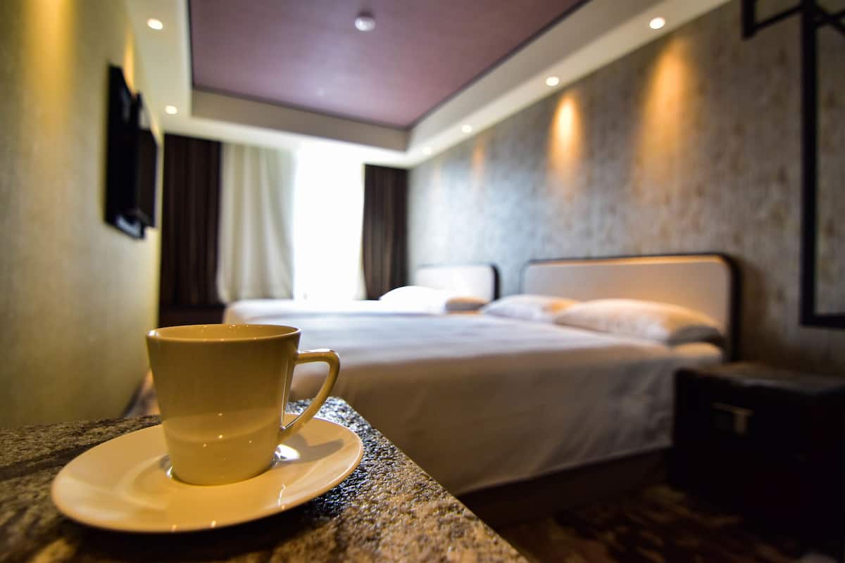 A hotel room with a bed, a cup on a saucer, and a nightstand.