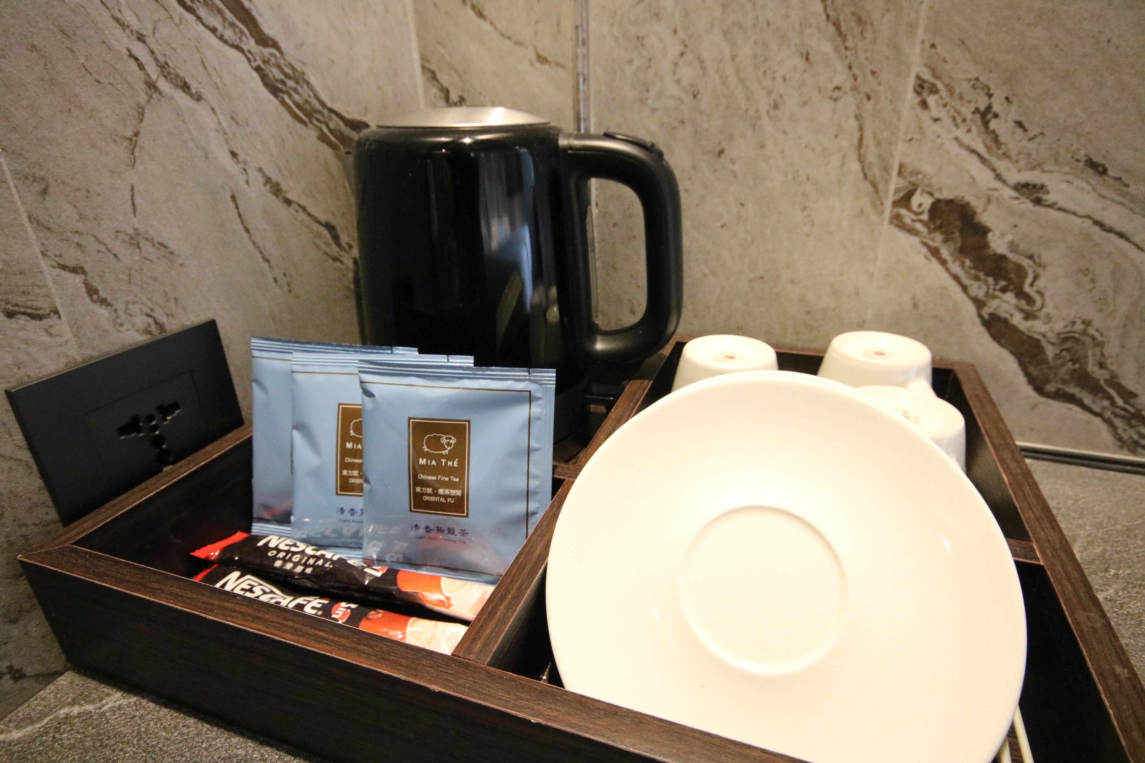 Un plateau avec une machine à café noire, une assiette blanche, deux rouleaux de papier toilette et deux sachets de café Nescafe.
