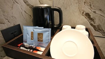 Un plateau avec une machine à café noire, une assiette blanche, deux rouleaux de papier toilette et deux sachets de café Nescafe.