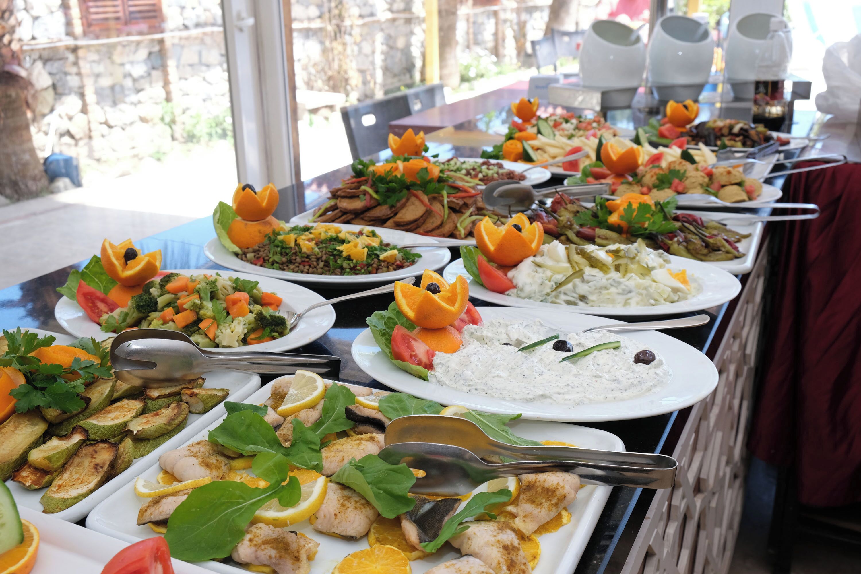 Una mesa de bufé con diversos platos, como ensaladas, arroz y pescado, dispuestos en fuentes blancas.