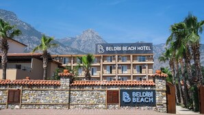 A hotel with a sign reading "BELDIBI BEACH HOTEL" and a stone wall with a sign below it. - Beldibi Beach Hotel (Kemer)