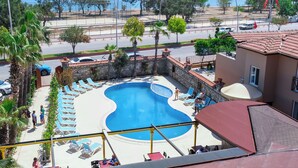 A swimming pool with lounge chairs, a stone wall, and a view of the sea. - Beldibi Beach Hotel (Kemer)