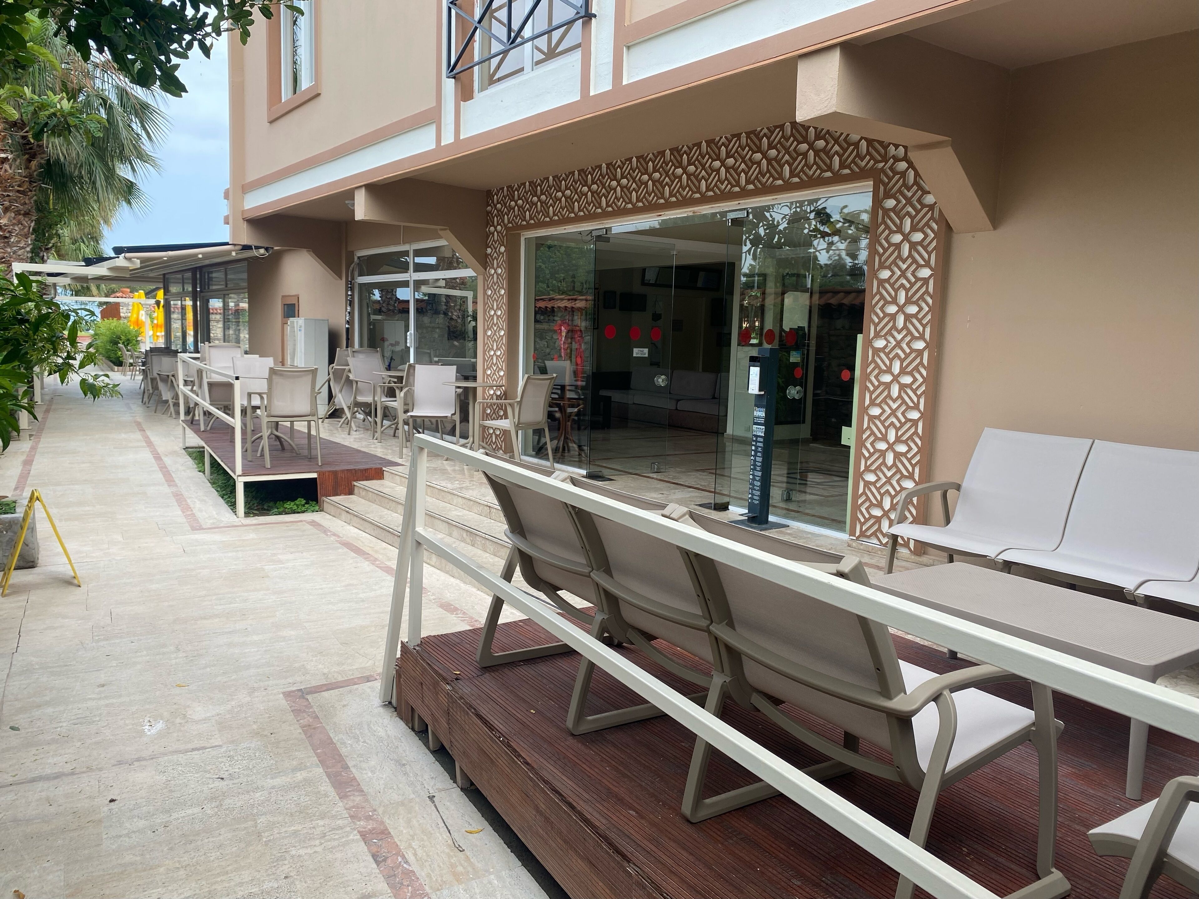 An outdoor seating area with tables and chairs, a wooden deck, and a glass entrance to the building.