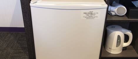 A compact refrigerator with a label, a hairdryer, and a kettle on a shelf.