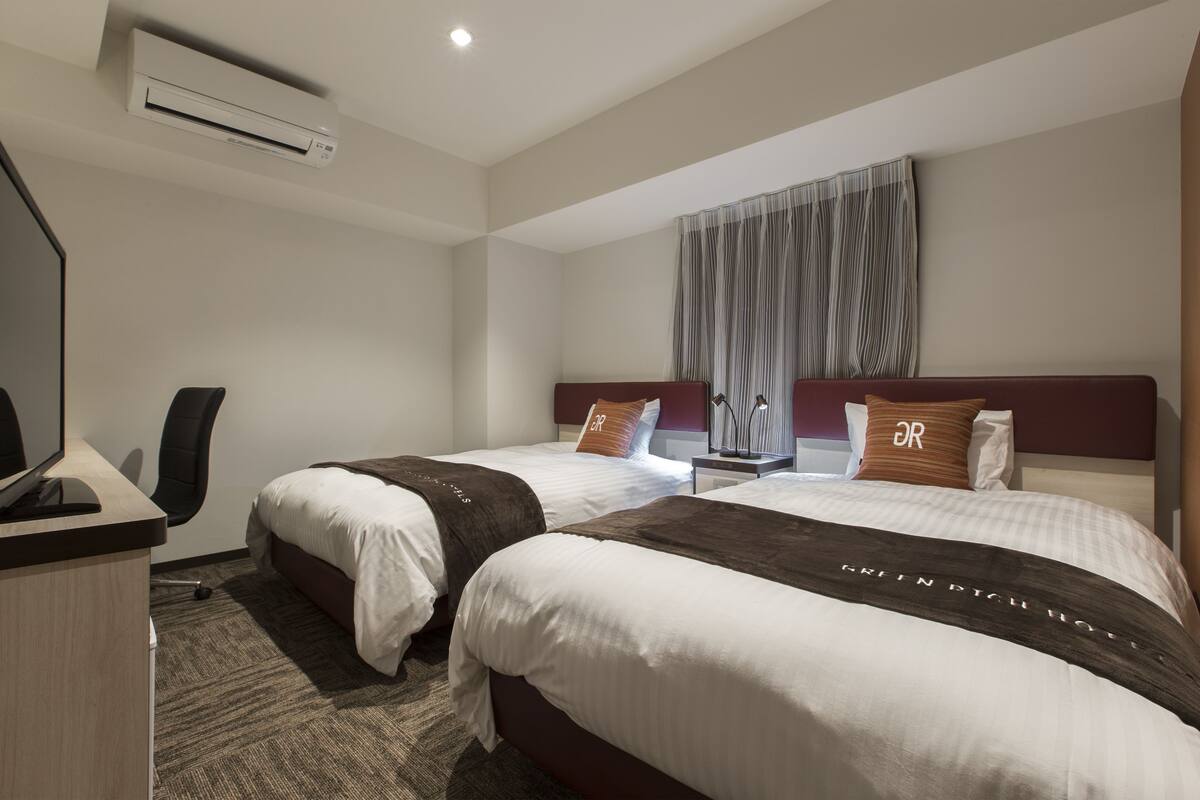 A hotel room with two beds, a desk, and a chair.
