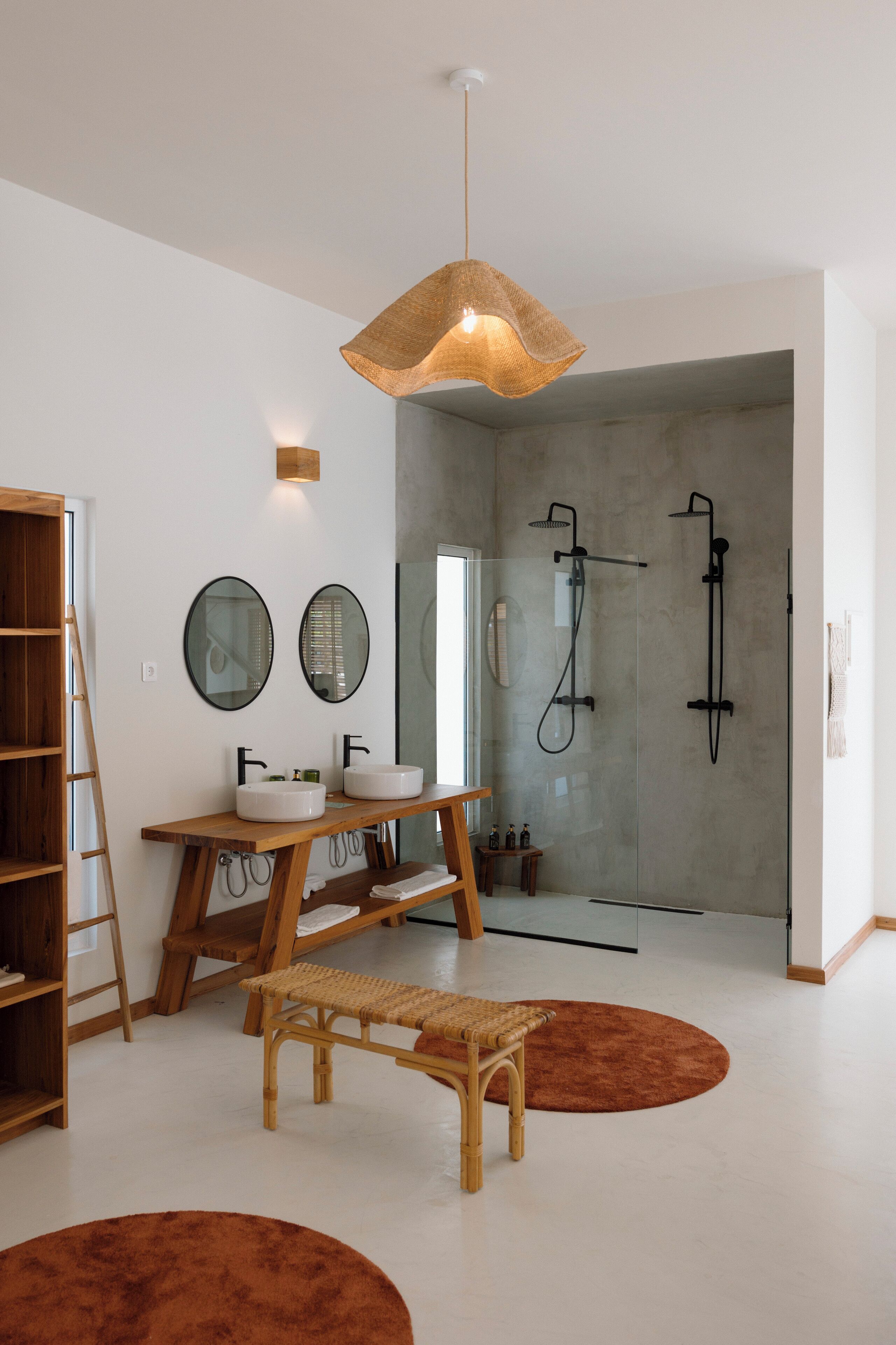 A modern bathroom with a glass shower enclosure, a wooden vanity with two sinks, and a hanging light fixture.