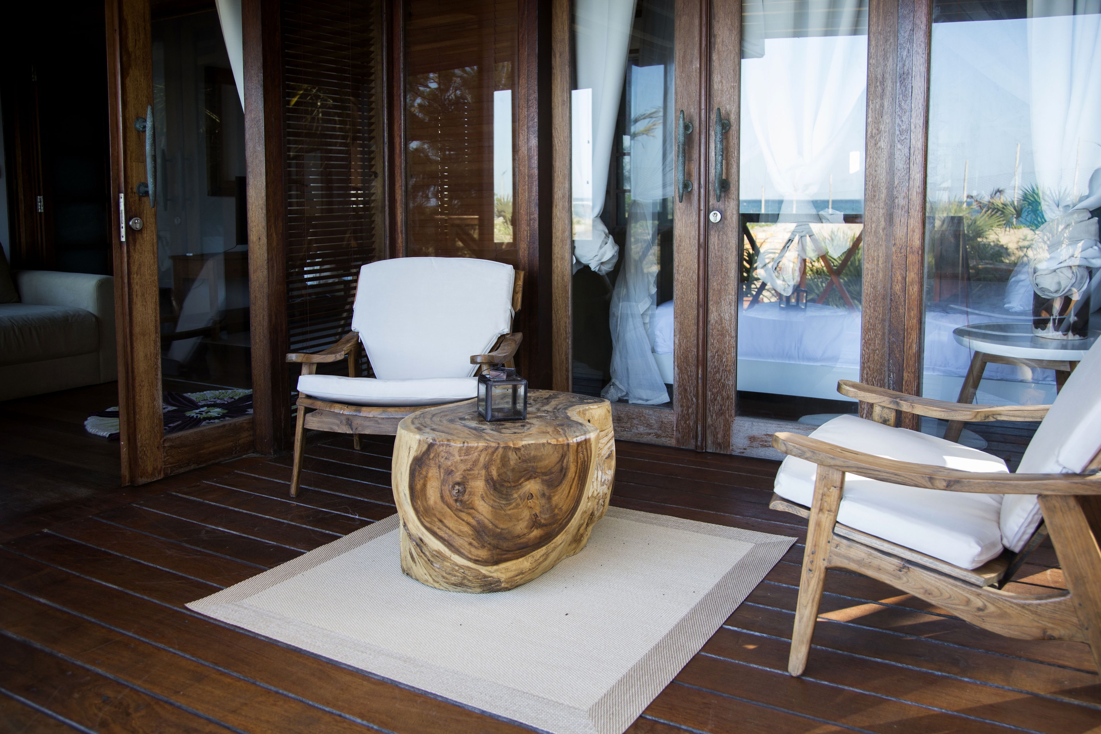 A wooden deck with a round wooden table and two white cushioned chairs.