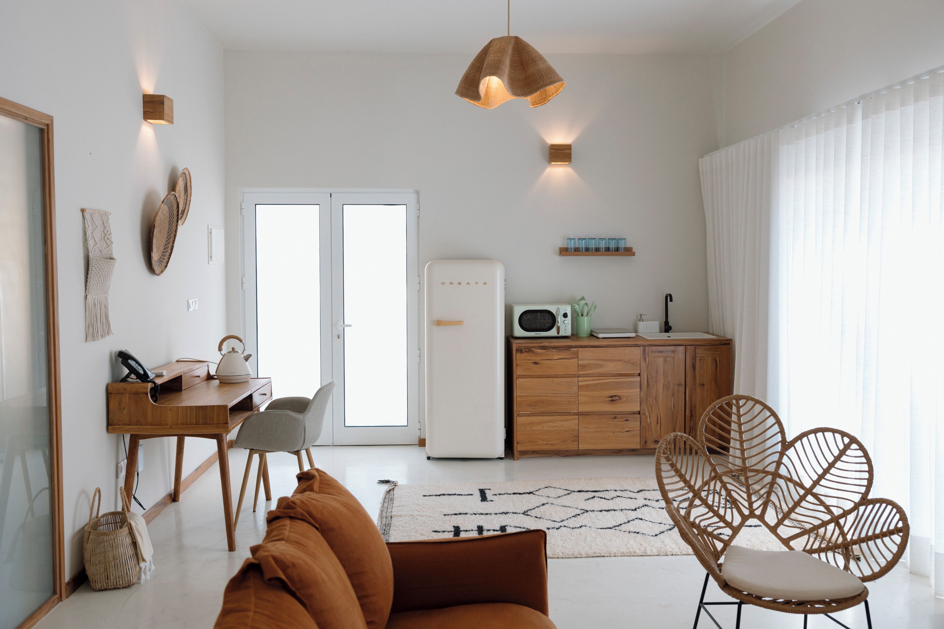 Una cocina moderna con refrigerador, microondas y gabinetes de madera. Hay un comedor con mesa y sillas, y una sala de estar con sofá y una silla decorativa.