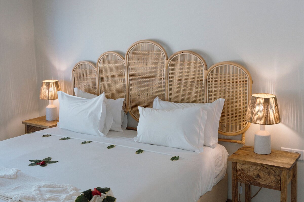 A neatly made bed with white linens and a decorative arrangement of leaves and flowers.