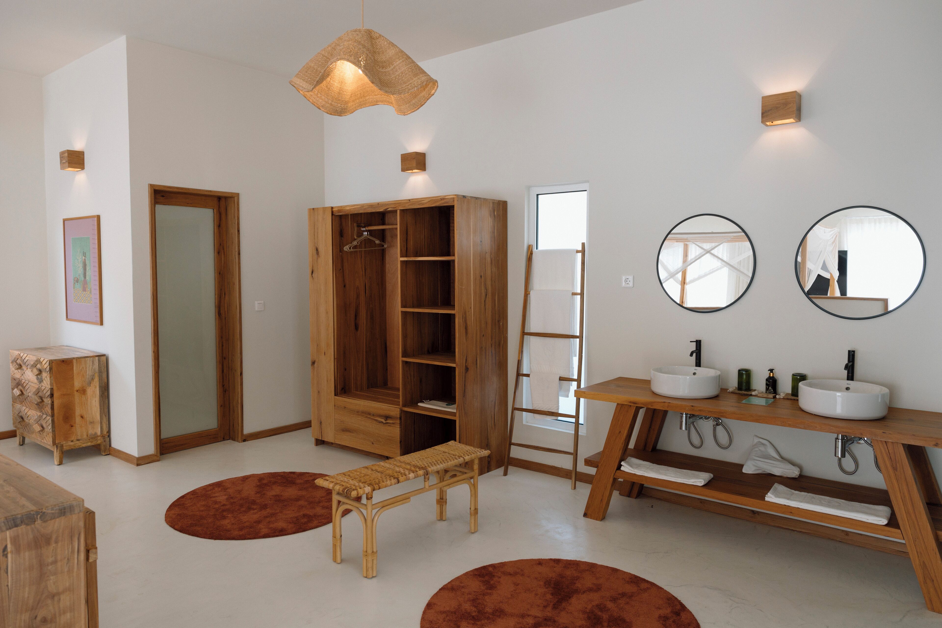 A modern bathroom with wooden cabinets, a bench, two sinks, and mirrors.