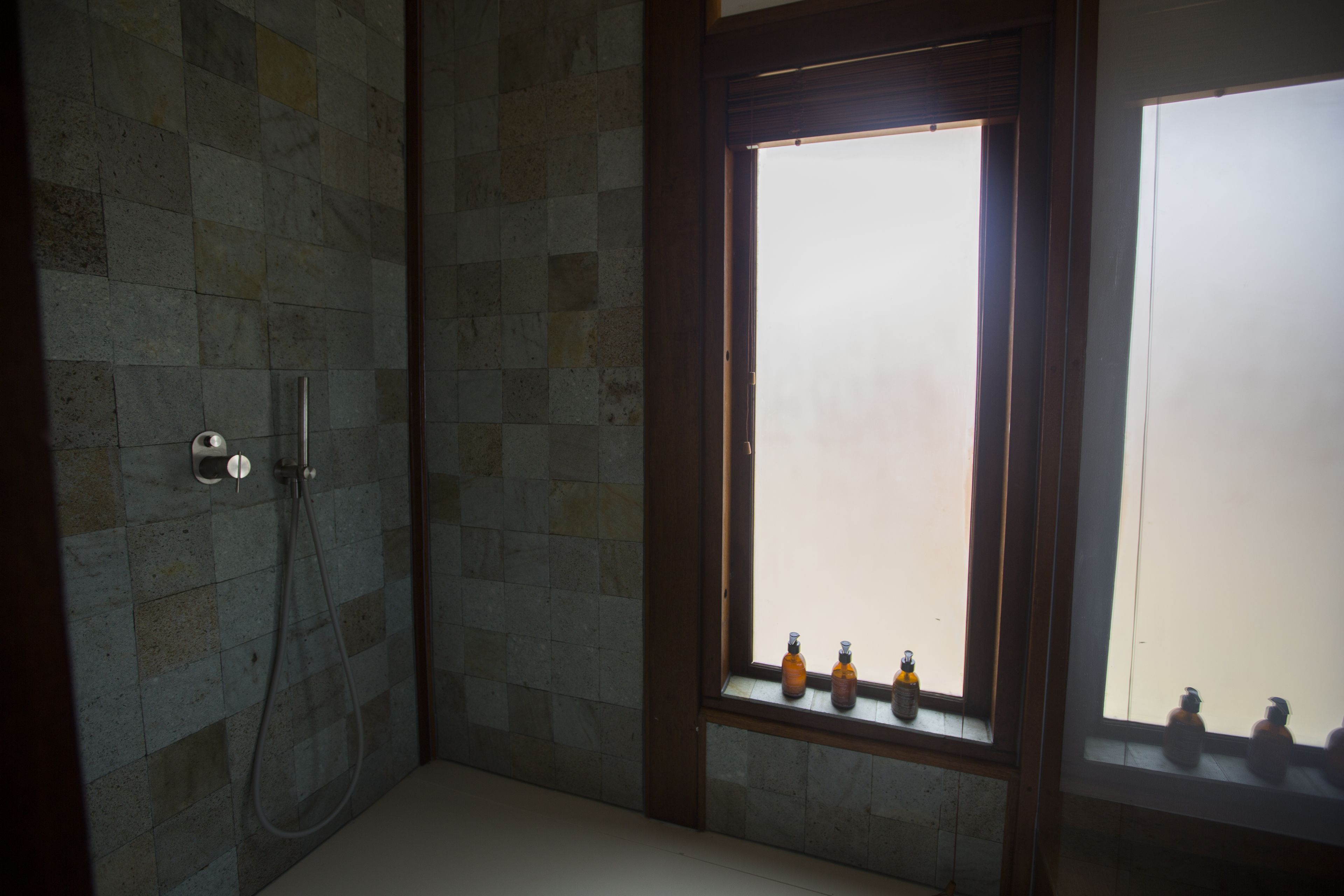 Une salle de bain avec une douche, une fenêtre sur le rebord de laquelle sont posées des bouteilles, et une vue à travers cette fenêtre.