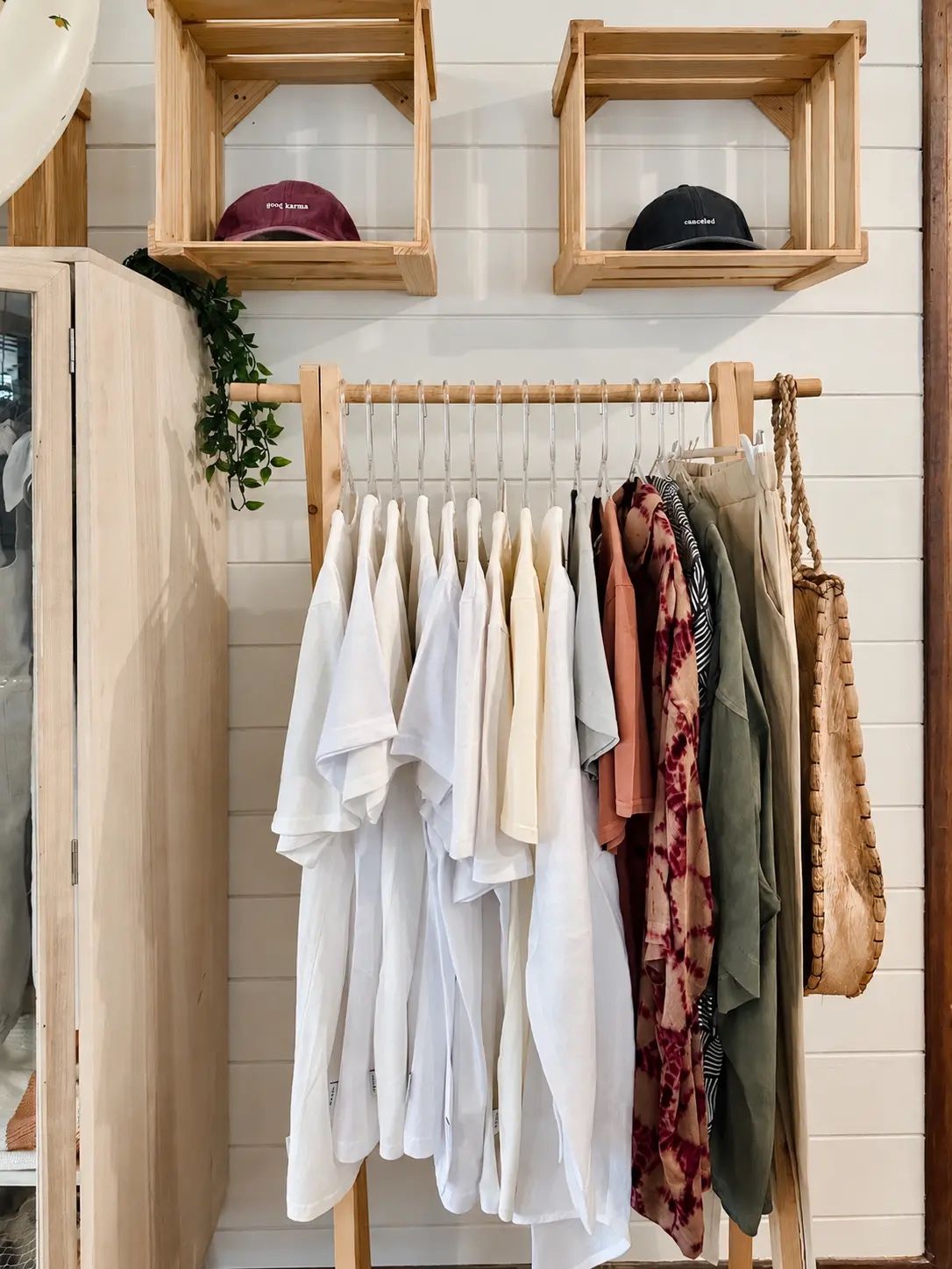 A clothing rack with various garments and a wooden shelf with hats.