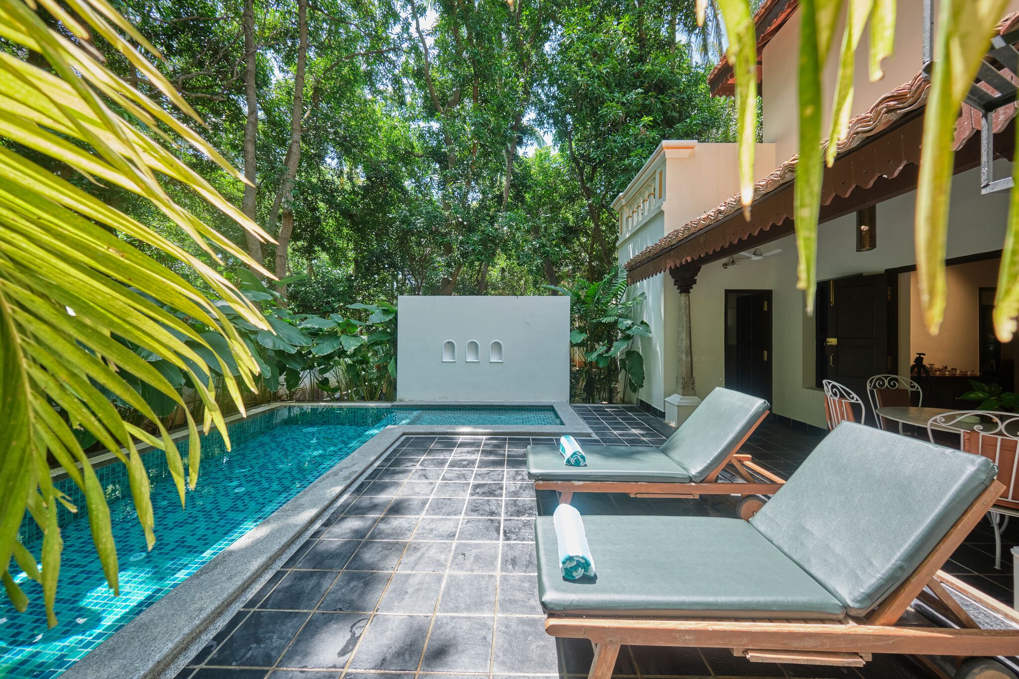 A pool area with lounge chairs, a tiled floor, and a building with a tiled roof.