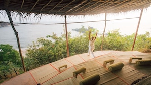 Una persona practicando yoga sobre una esterilla al aire libre, con vista al mar y a la vegetación.