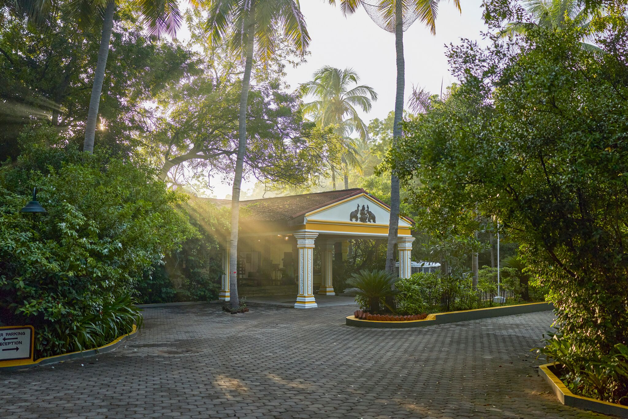 A paved courtyard with a building featuring a central columned structure and a sign indicating a parking area.