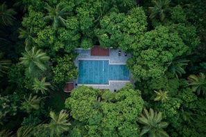 Eine Vogelperspektive zeigt ein Resort mit einem zentralen Schwimmbad, umgeben von üppiger tropischer Vegetation.
