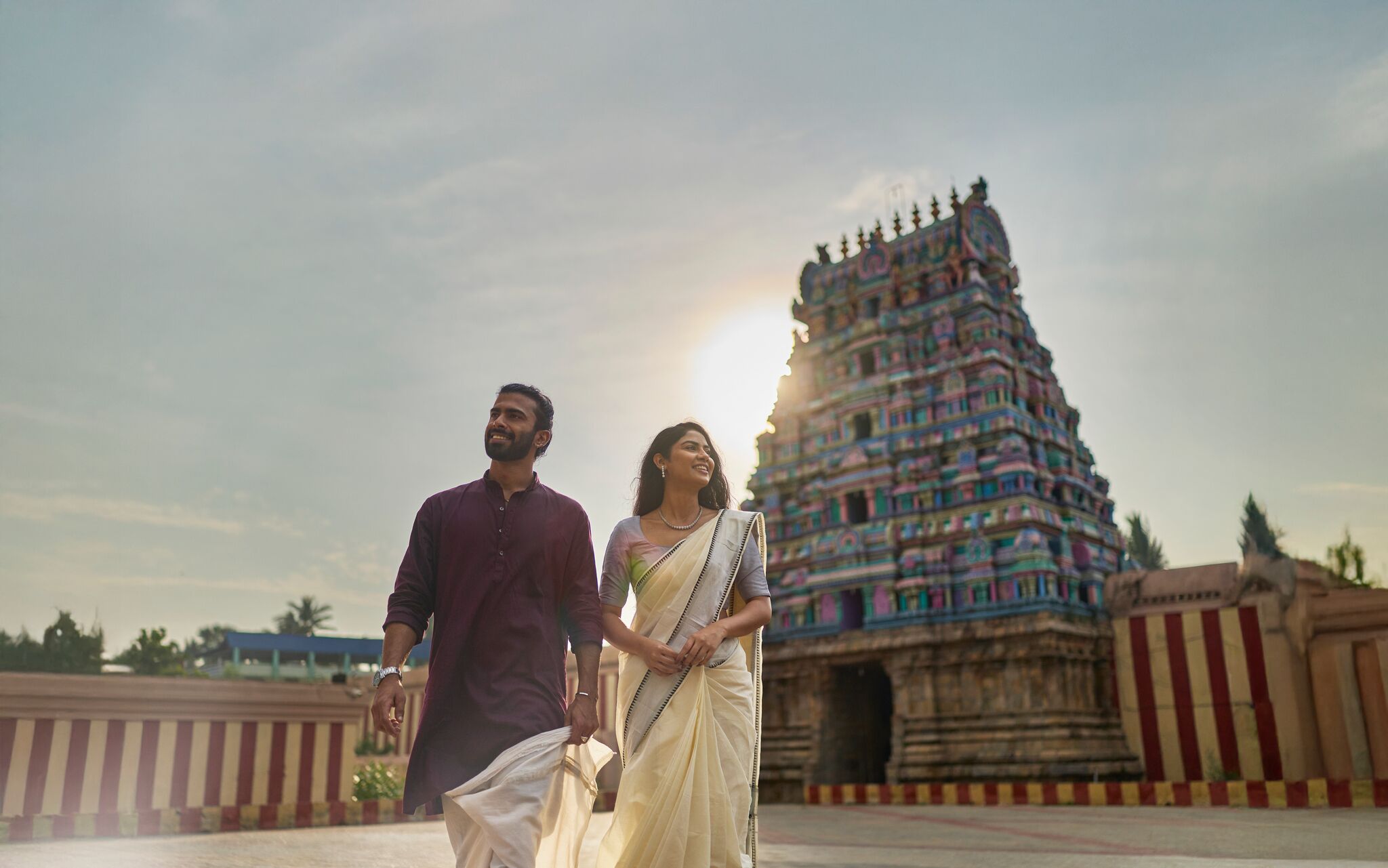 A couple walking in front of a temple with a tiered, colorful structure.