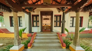 Una escalera conduce a una habitación con puerta de madera, flanqueada por columnas y plantas.