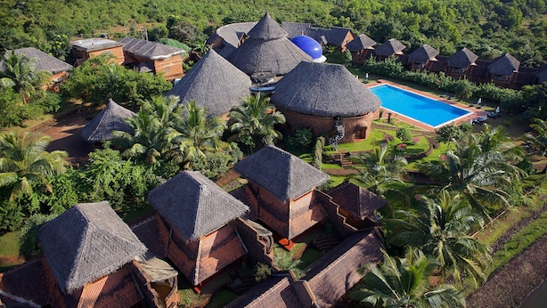 Vista aérea de un resort con cabañas de techo de paja, una piscina y abundante vegetación.