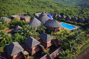 An aerial view of a resort with thatched-roof huts, a swimming pool, and lush greenery. - Swaswara- Cgh Earth (Kumta)