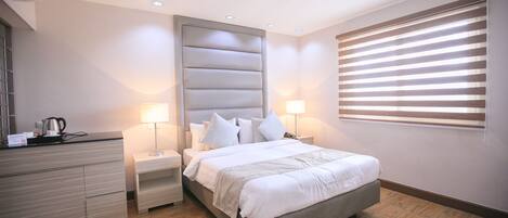 A modern bedroom with a bed, nightstands, a dresser, and a window with blinds.