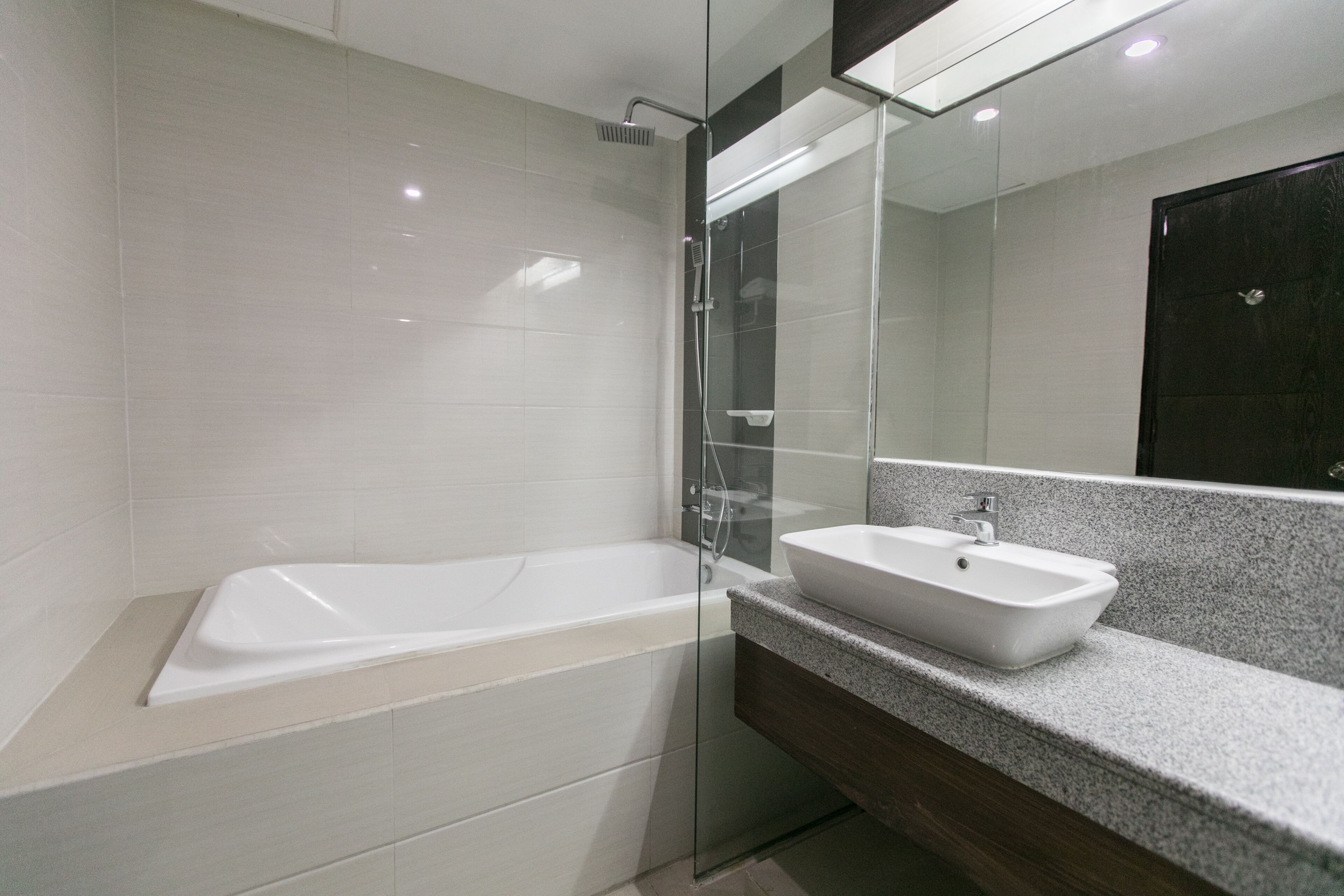Un baño moderno con ducha envuelta en vidrio, una bañera blanca y encimera de granito con lavabo blanco.