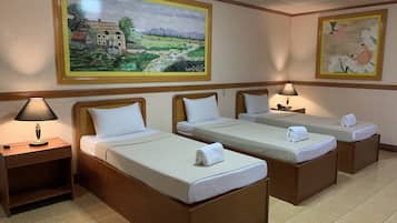 A hotel room with two single beds, a nightstand, a lamp, and two paintings on the wall.
