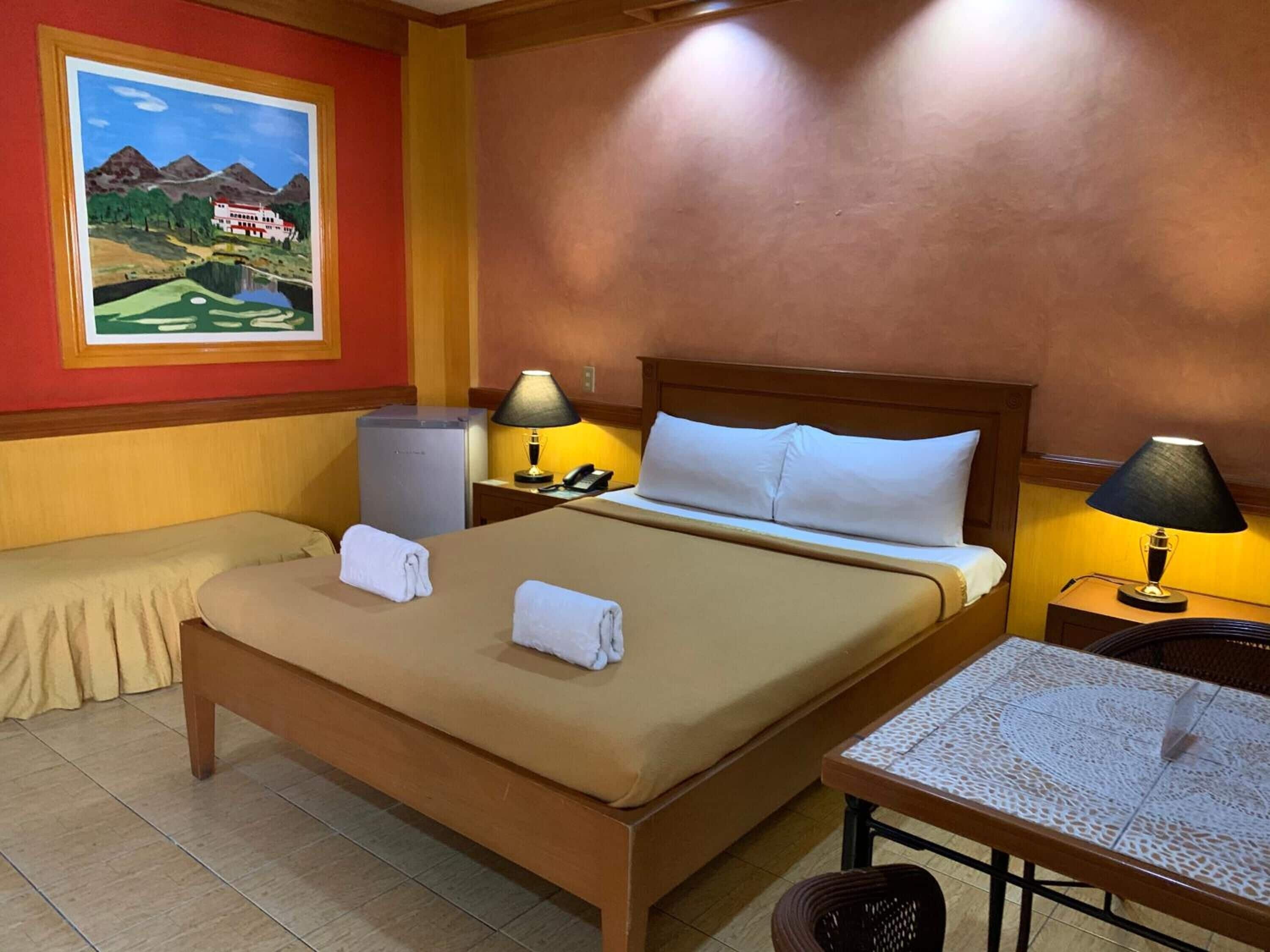A hotel room with a large bed, two bedside tables with lamps, a small table, and a painting on the wall.