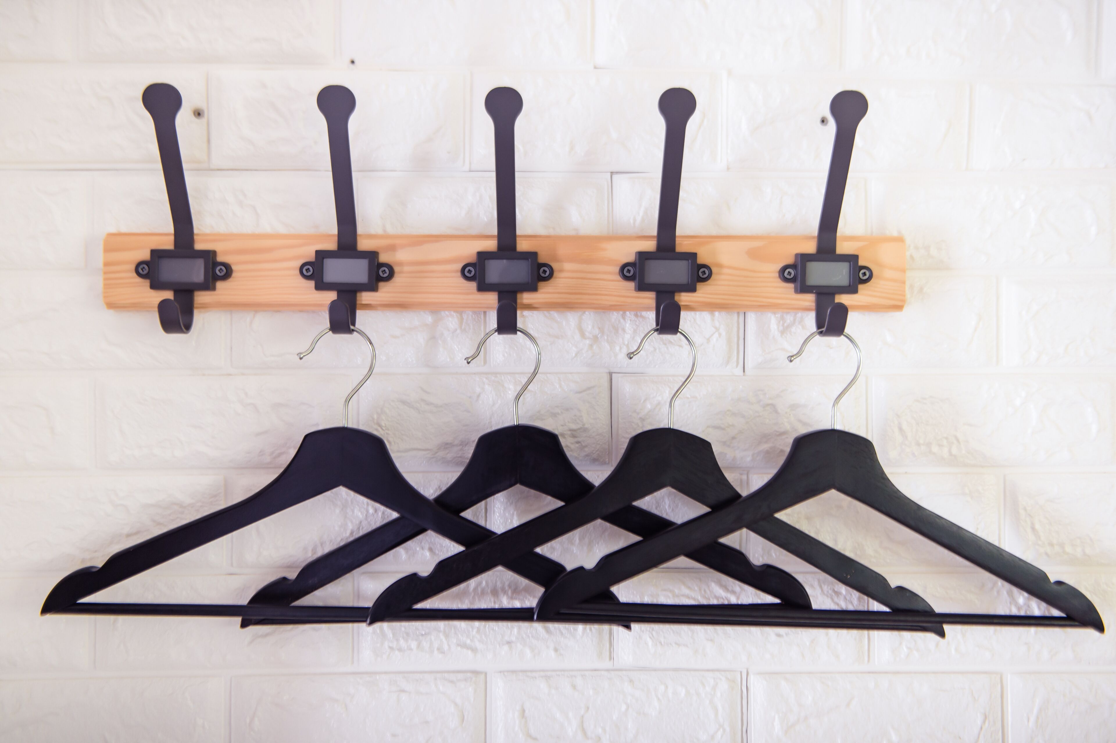 A wall-mounted coat rack with five hooks and a wooden panel above it.