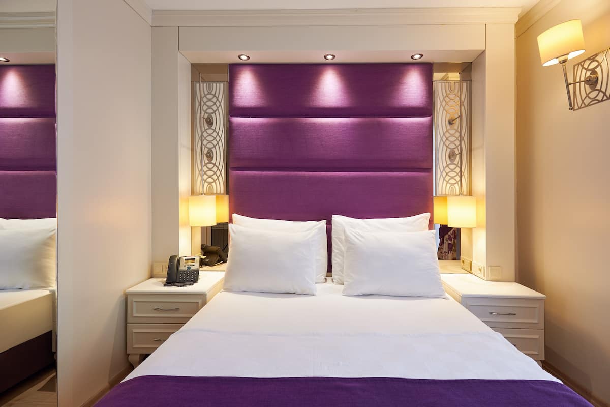 A hotel room with a large bed, two bedside tables, a telephone, and decorative wall sconces.