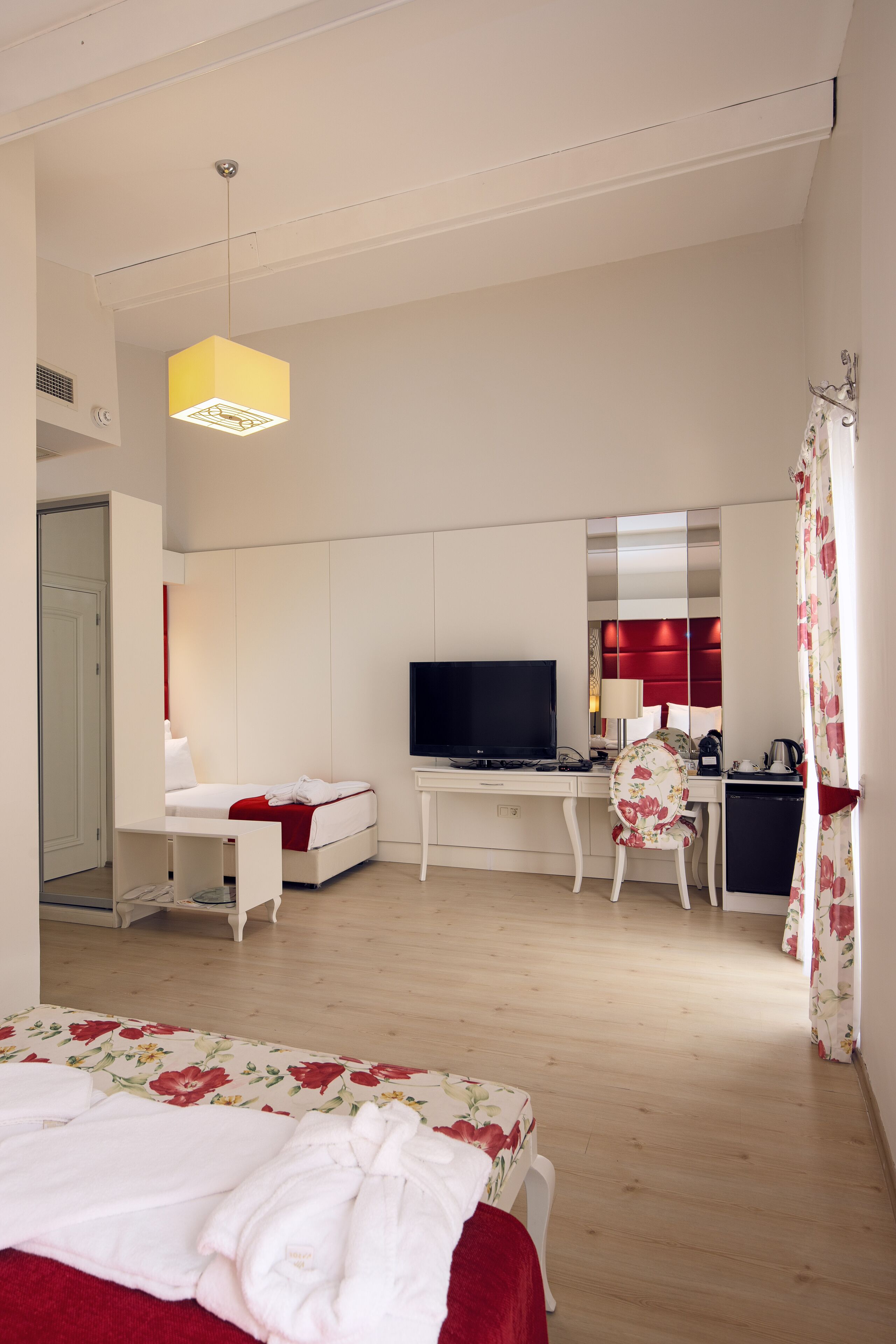 A hotel room with a bed, a desk with a flat-screen TV, a chair, a small table, and a mirror.