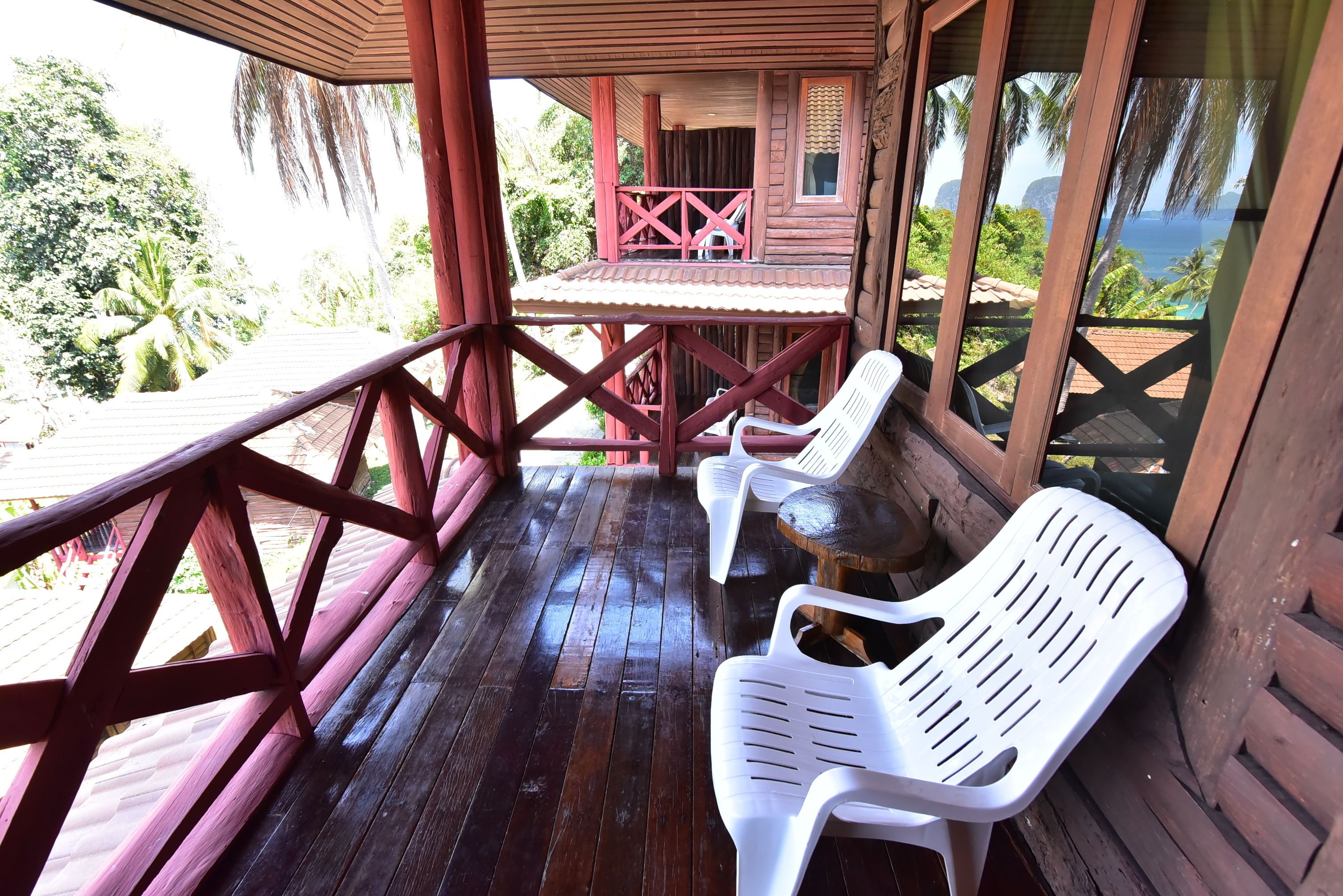 A wooden deck with a wooden railing, a table, and two white plastic chairs.
