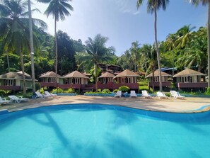 A pool area with lounge chairs and overwater bungalows surrounded by palm trees. - Koh Ngai Resort Trang (Ko Lanta)
