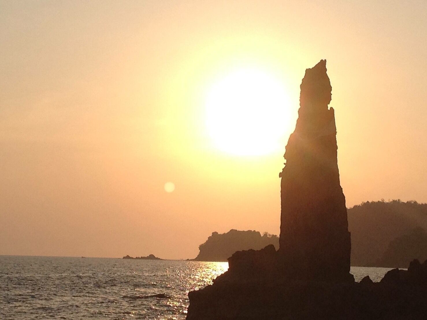 A coastal sunset with a prominent rock formation silhouetted against the sky.