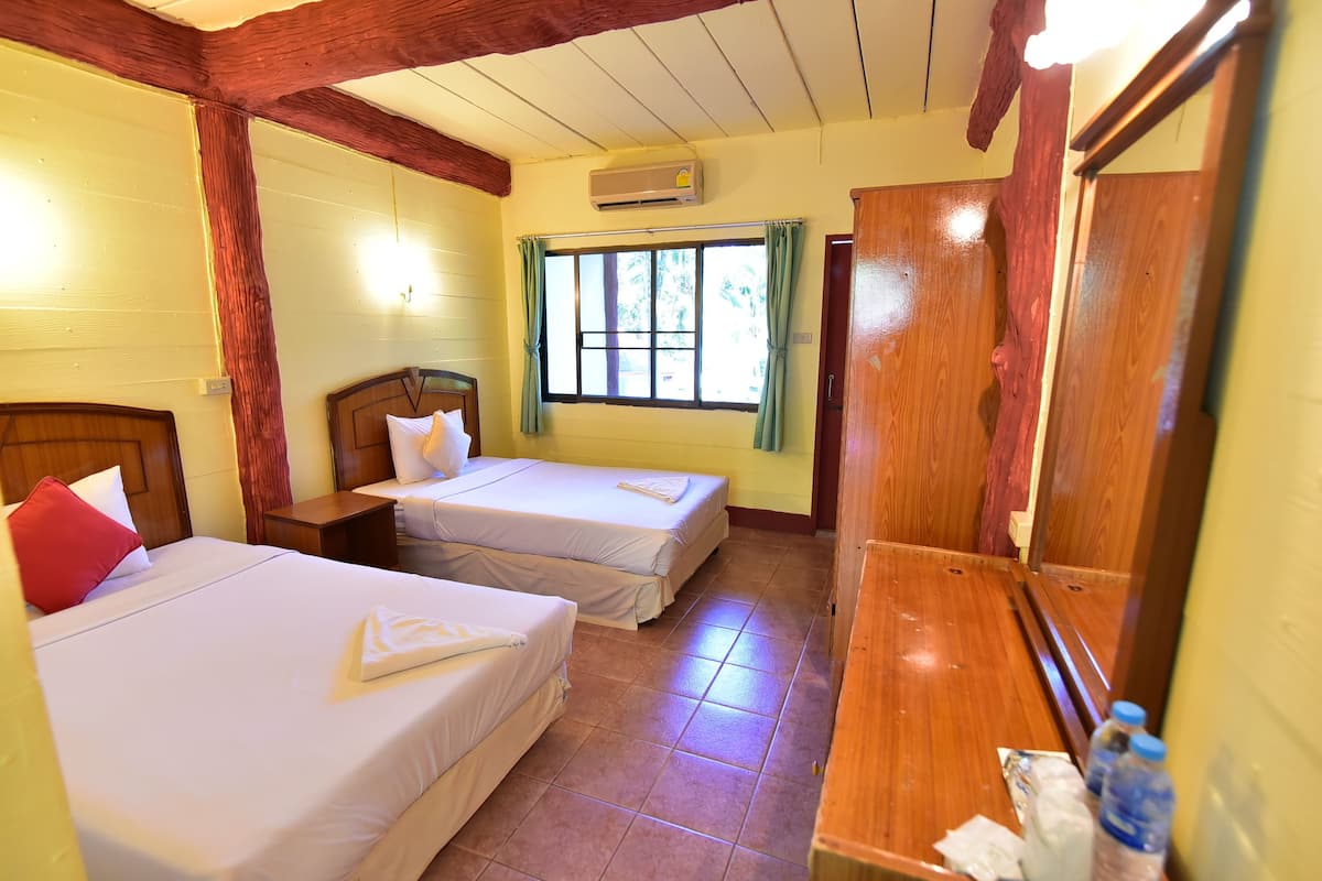 A room with two beds, a wooden wardrobe, a window with curtains, and an air conditioning unit.