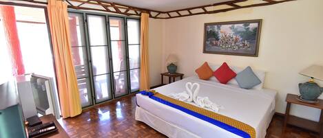 Una habitación de hotel con cama, escritorio con computadora, televisor y ventana con cortinas.