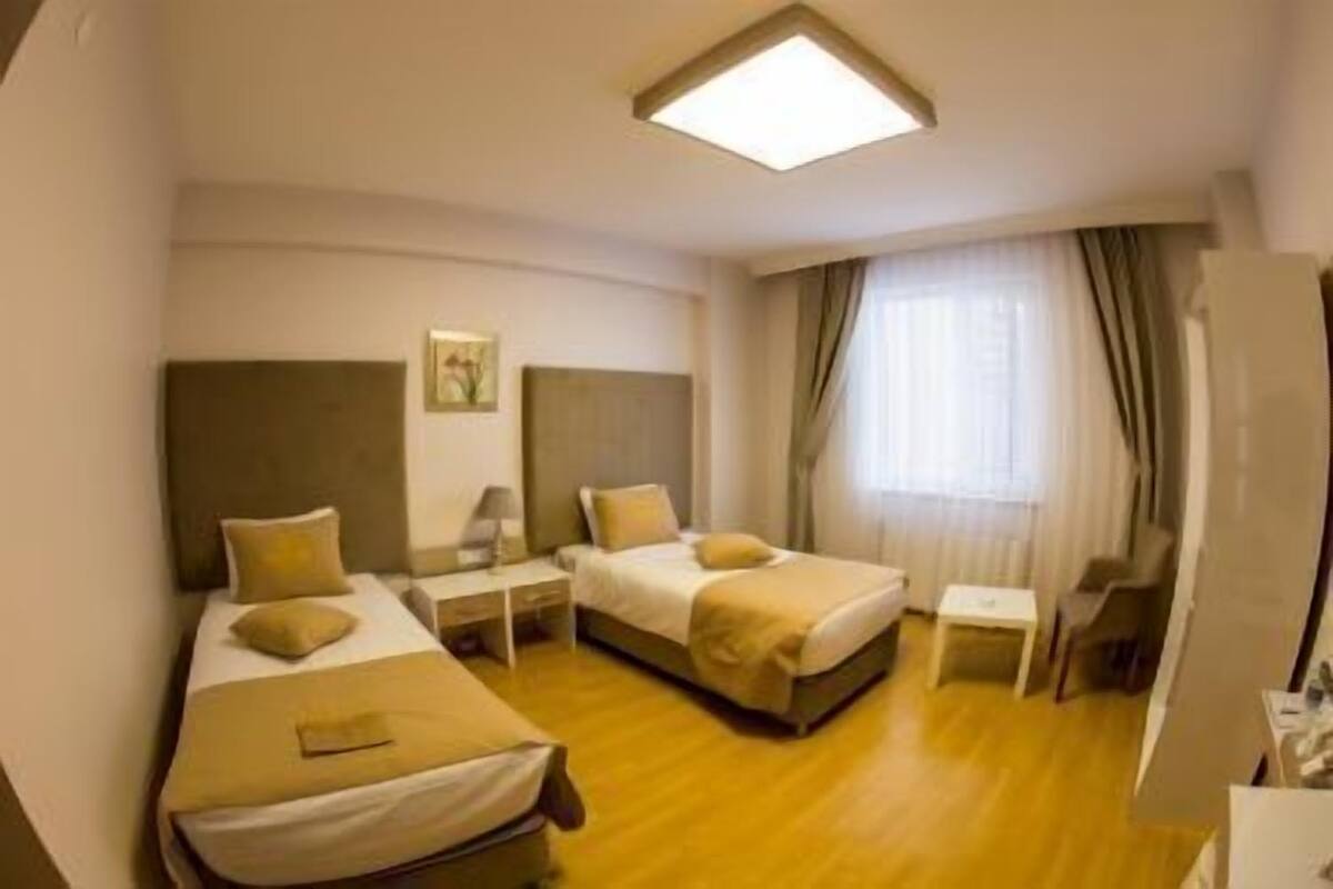 Ein Hotelzimmer mit zwei Betten, einem Nachttisch mit Lampe, einem kleinen Tisch und einem Fenster mit Vorhängen.