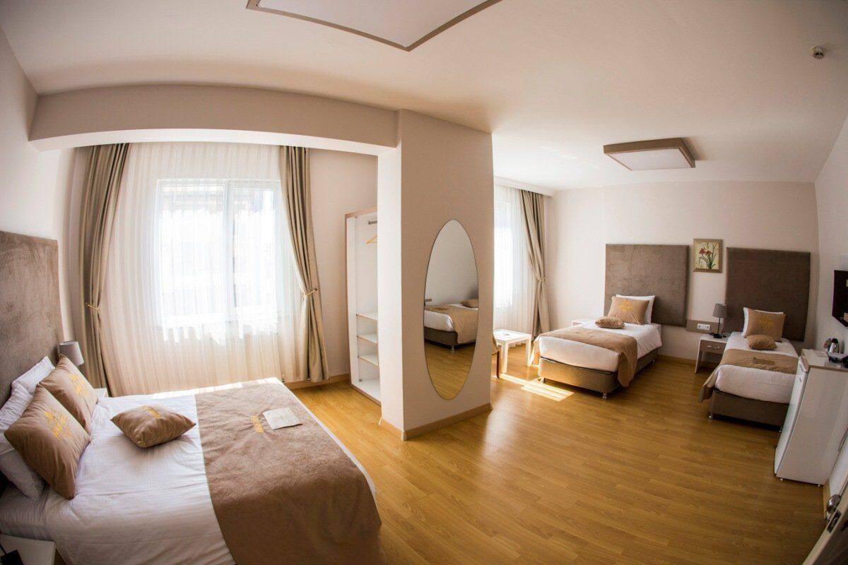 Ein modernes Hotelzimmer mit einem großen Bett, zwei Einzelbetten, einem Schreibtisch und einem Kleiderschrank.