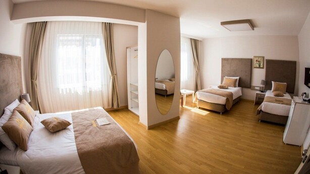 A modern hotel room with a large bed, two smaller beds, a desk, and a wardrobe. - Bilge Suite Hotel (Corum)