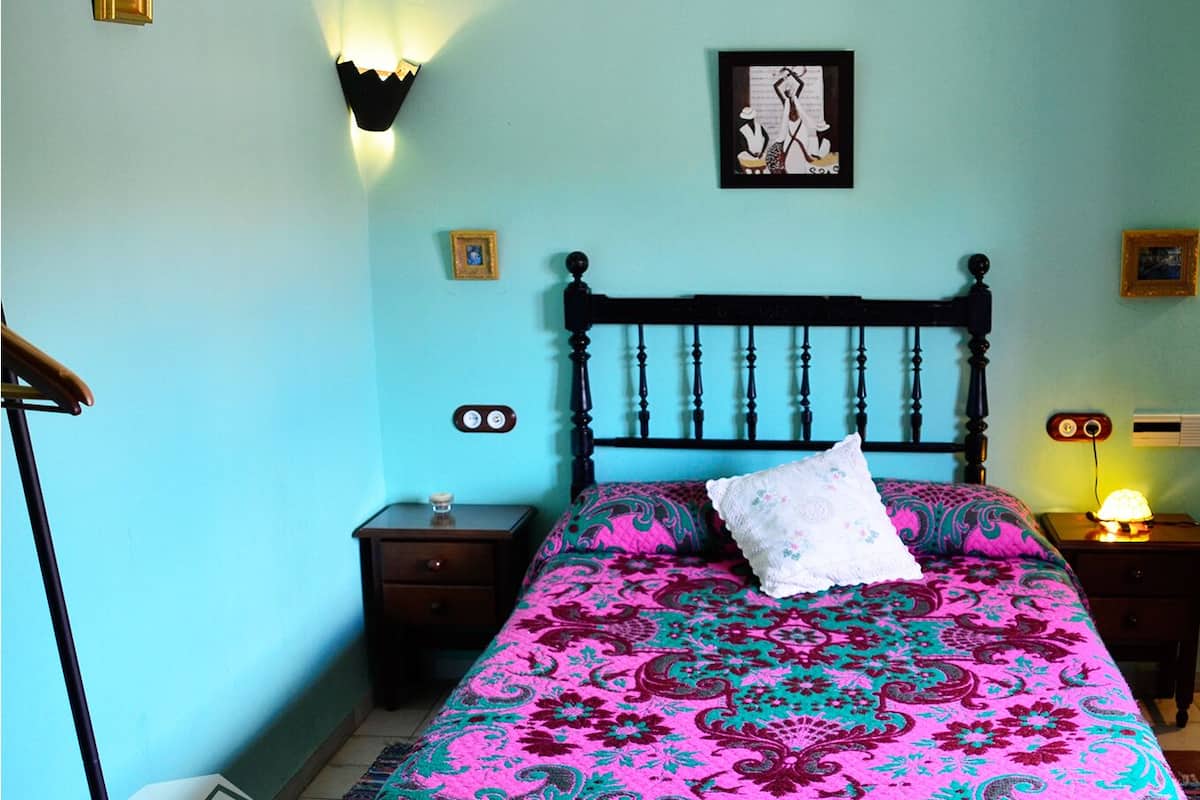A bedroom with a bed, two bedside tables, a nightstand, and a wall-mounted lamp.