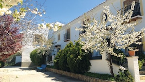 A building with a white facade, multiple windows, and balconies. There is a bench and a potted plant in the foreground. - Molino de Morillas (Galera)