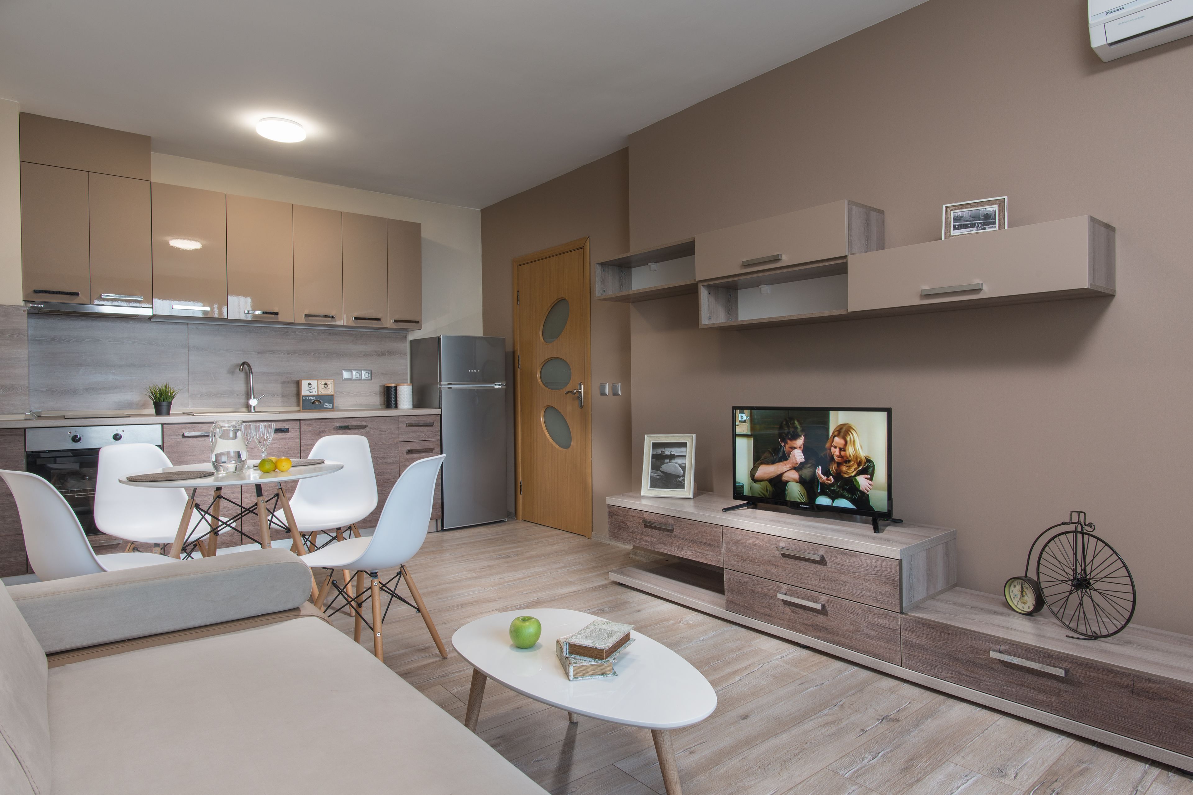 Un salon moderne avec un canapé, une table basse et un téléviseur. Il y a également un coin cuisine équipé de placards et d’un réfrigérateur.