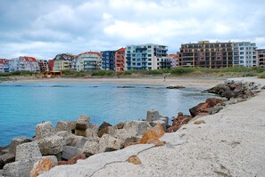 Una zona costera con playa, costa rocosa y edificios coloridos al fondo.