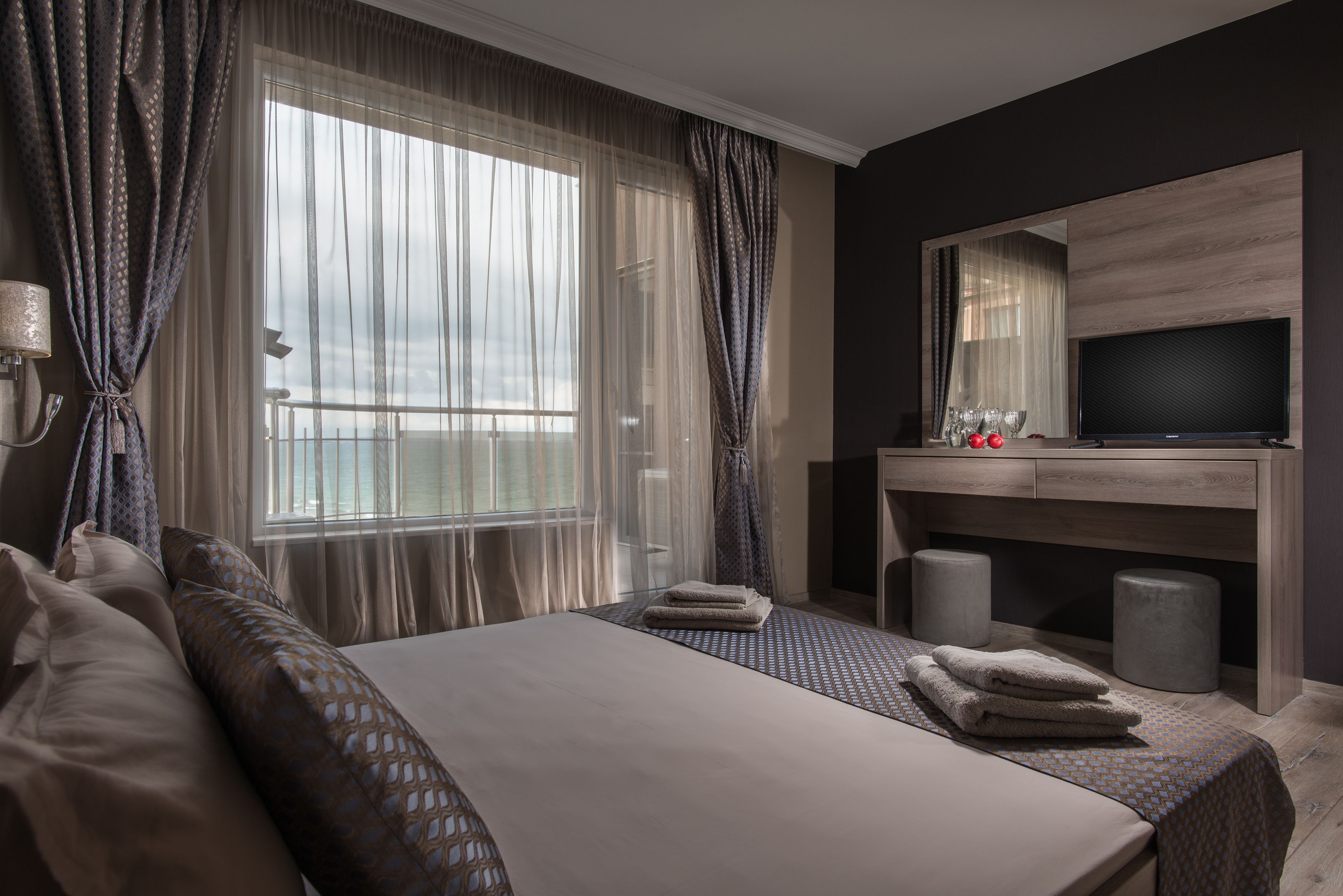 A hotel room with a large bed, a TV, a desk, and a window with curtains.