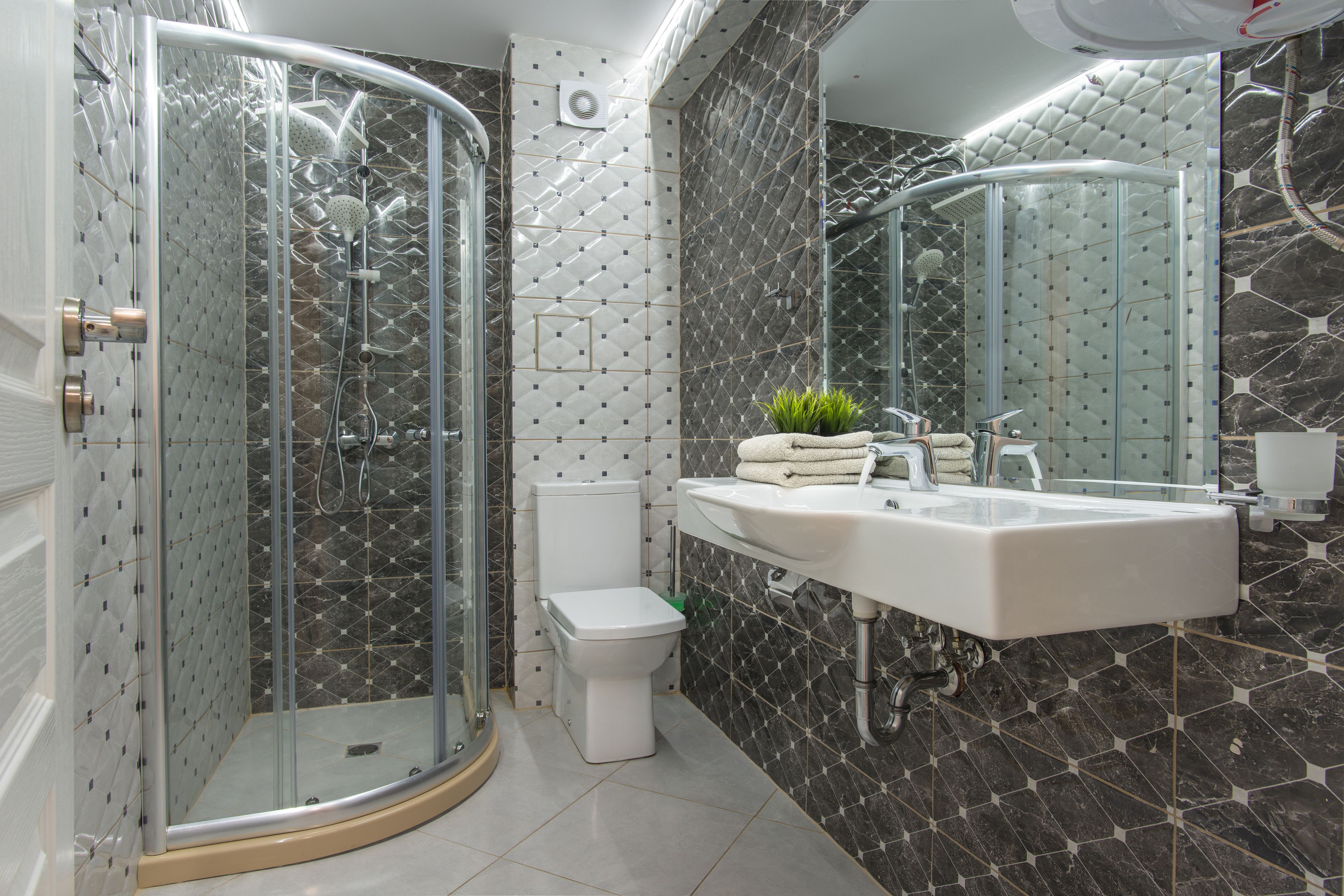 A modern bathroom with a glass-enclosed shower, a toilet, and a sink with a mirror above it.