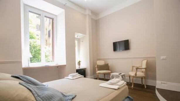 A bedroom with a bed, two chairs, a TV, and a window. - Relais della Torre (Rome)