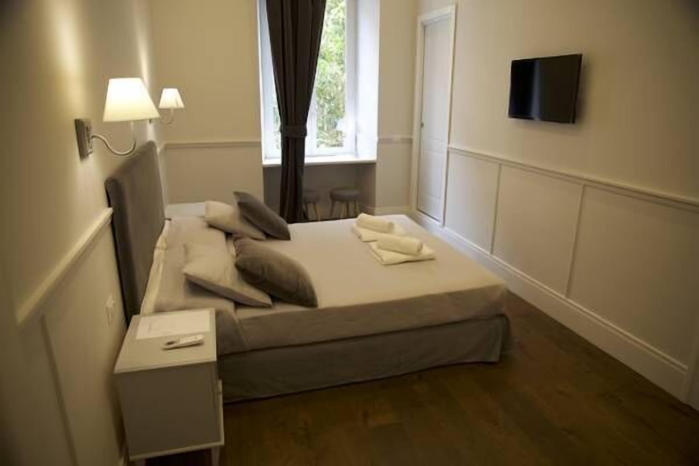A bedroom with a bed, bedside tables, a TV mounted on the wall, and a window with curtains.