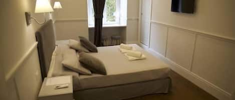 A bedroom with a bed, bedside tables, a TV mounted on the wall, and a window with curtains.