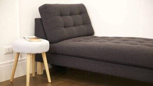 A modern room with a grey sofa, a small white stool, and a wooden floor. - Relais della Torre (Rome)