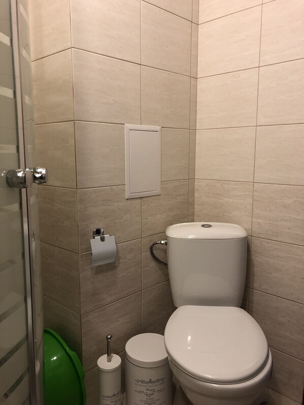A bathroom with a toilet, a green trash bin, and a paper towel dispenser. - Palace Deluxe Hotel (Pomorie)